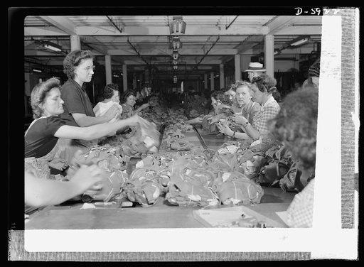 Women in industry. Gas mask production. The finished gas mask face pieces in the foreground were just flaps of rubber without eye pieces, outlet valves, straps, tabs, and other accessories when they started on the long moving belt at the far end of the line. By the time they've reached this end, how