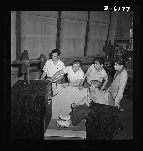 Training high school boys to identify planes. These high school boys constructed this trainer plane, and the young man holding the stick is operating it. Note the instruments and control board. This is one phase of the aviation course offered boys at the Weequahic High School in Newark, New Jersey