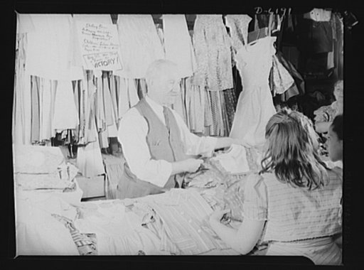Posting ceiling prices in foreign languages. The plea to "Buy United States War Stamps and Bonds for Victory," which completes the ceiling price sign, emphasizes the patriotic spirit shown by O. Schwartz, proprietor of a children's dress stand in one of New York's East Side marketplaces. Mr. Schwart