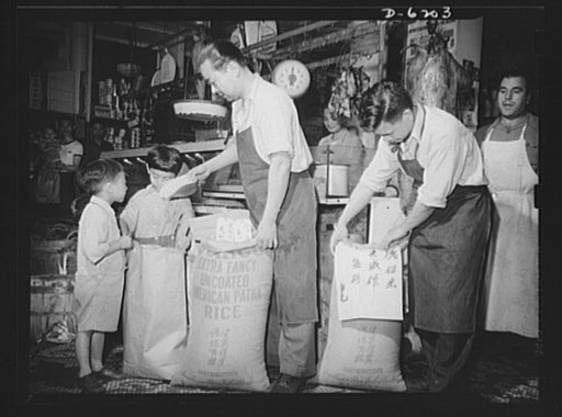Posting ceiling prices in foreign languages. In a large store in the heart of New York's Chinatown, manager Lee Bow, at right, is attaching a price ceiling sign to a sack of rice so that his customers will easily understand his maximum prices for this commodity. Clerk Eng Hong pours rice with the he