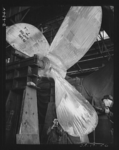 Production. Ship propellers, etc. Balancing a giant ship propeller is a difficult job that must be done accurately. Two workmen, their eyes protected by goggles, chip away areas of the manganese bronze blades so that the power of the ship may be put to work efficiently. Baldwin Locomotive Works