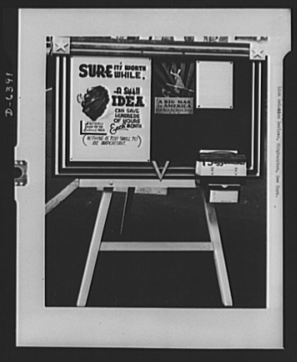 A bulletin board serves as a central source of up-to-date war production drive information at Link Aviation Devices, Binghamton, New York. A poster urges employees to contribute ideas for speeding up production. A lunch box painted in red, white and blue is used for suggestions