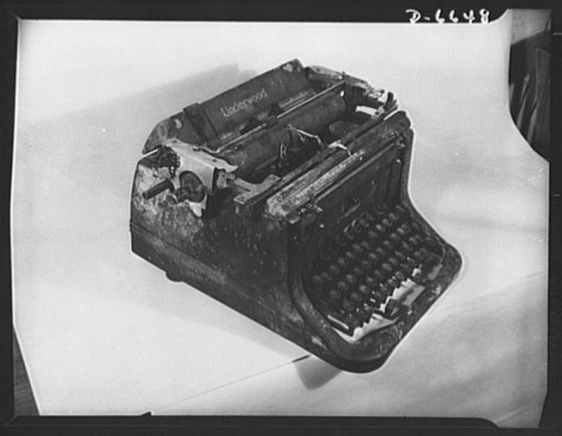 Battle-scarred typewriter. Veteran of World War II, this typewriter has been through a Japanese bombing at sea. Everything in the room in which it was located was completely demolished except the typewriter, including the table on which it was standing. Note damaged carriage--the result of a bomb