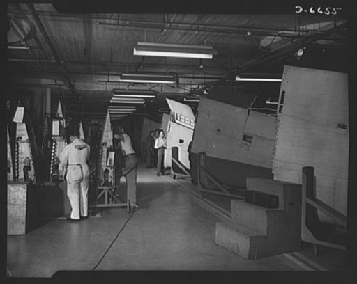 Production. Lockheed P-38 pursuit planes. Final inspection and rework on wings for Lockheed P-38 pursuit planes in a large Western aircraft plant. The wings, which had been accurately assembled in jigs, are joined to the plane bodies as they travel down the final assembly line where engines, landing