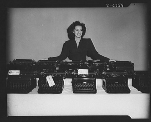 The stories they've told! Another load of RKO Radio typewriters is turned in to the government for war work. Somewhere in the lot is Maureen O'Harra's personal typewriter which she added to the pile before she would pose in the picture. The machines come from the script department where each one has