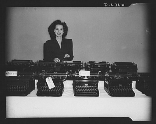 The stories they've told! Another load of RKO Radio typewriters is turned in to the government for war work. Somewhere in the lot is Maureen O'Harra's personal typewriter which she added to the pile before she would pose in the picture. The machines come from the script department where each one has