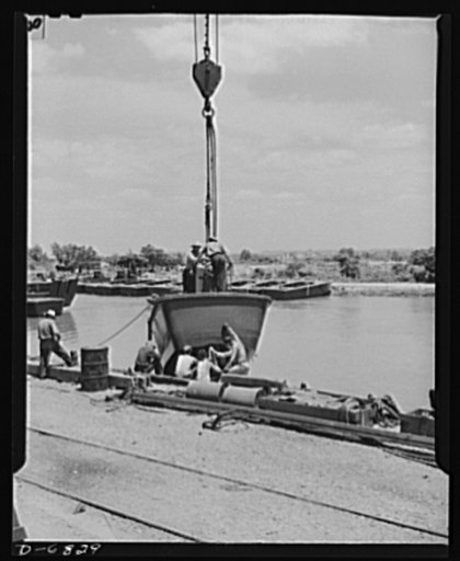 Production. Ramp boats. Launching a wooden ramp boat by crane at a Southern shipyard. These twenty-six-foot carriers, built of prefabricated sections, are used for making beach landings of men and equipment. They are delivered from the shipyard in tows of six to eight boats. Higgins Industries