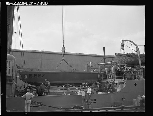 Production. Small ramp boats. A new wooden ramp boat, just completed at a Southern shipyard, is swung aboard a freighter for delivery to the Navy. The bottom-hinged sterns [i.e. bows] of these boats are used as ramps to make fast, dry landings of men and equipment at beach locations of any kind. Hig