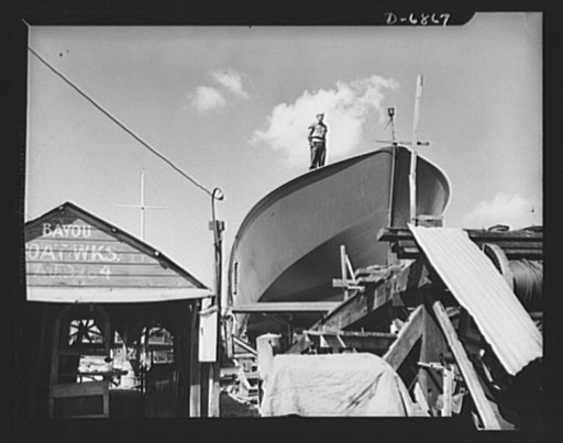 Production. Motor torpedo boats (wooden). A Coast Guard sentry stands watch over a new torpedo boat under construction at a Southern shipyard. In addition to wooden torpedo boats, the yard also turns out many steel boats for the Navy. Higgins Industries
