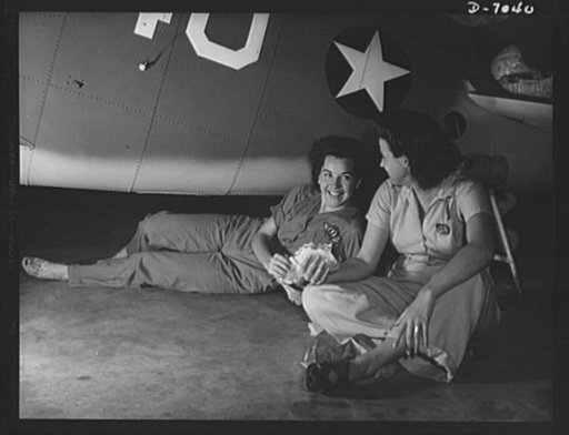 Naval air base, Corpus  Christi, Texas. War-time luncheon "under the shade of ....a Navy plane. These women workers held man-size jobs in the Assembly and Repair Department at the Corpus Christi, Texas, naval air base. Slack suits and coveralls take the place of afternoon frocks for these workers