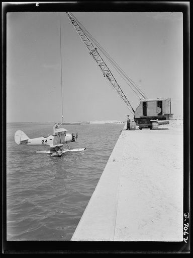 Naval air base, Corpus Christi, Texas. Hooked to a derrick, a Navy N3N plane is made ready for hoisting out to shore onto a "dollie." The plane is then wheeled back to the assembly and repair department of the naval air base at Corpus Christi, Texas, for reconditioning by civil service mechanics