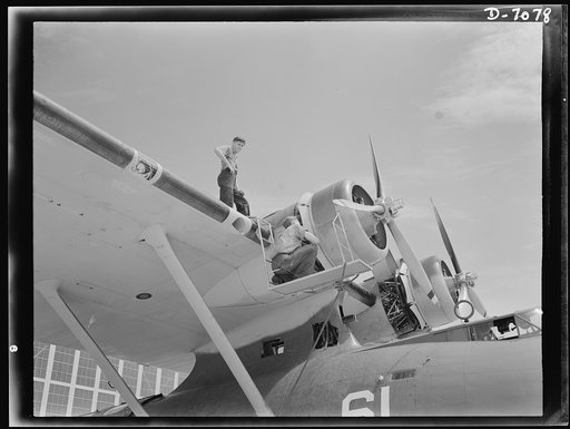 Naval air base, Corpus Christi, Texas. Perched at the nose of a Navy PBY flying ship, two sailors check the huge motor to keep them in first class condition while the plane is in service. These men are aviation mechanics nates stationed at the Naval Air