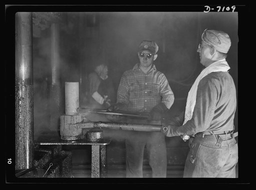 Production. 105 millimeter shells. This red-hot billet is undergoing processing in a hydraulic press, where it will be pierced and drawn into the rough shape of an artillery shell. In pre-war days, plumbing fixtures were processed in this Midwest factory (Manitowac Shipyards)