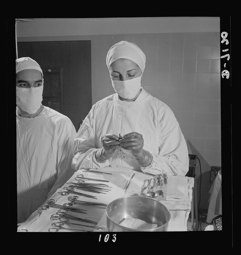 Nurse training. Calm and dependable in emergency situations, a student nurse threads a suture in a needle, first step in preparation for a tracheotomy