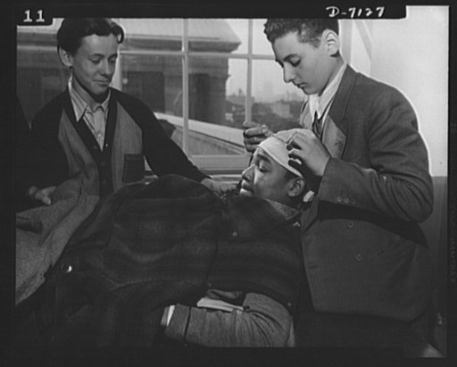 High school Victory Corps. The grimace of the "victim" lends reality to the first instruction these boys receive at Benjamin Franklin High School in New York City. One day a week they take time out from their English course for "war activities", and learn the basic principles of first aid
