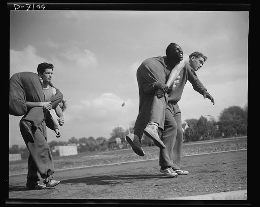 High school Victory Corps. The fireman's "carry." The correct method of carrying a wounded comrade, is shown here by some of the boys in the  "commando" course which is part of the physical education program of Flushing High School, Queens, New York