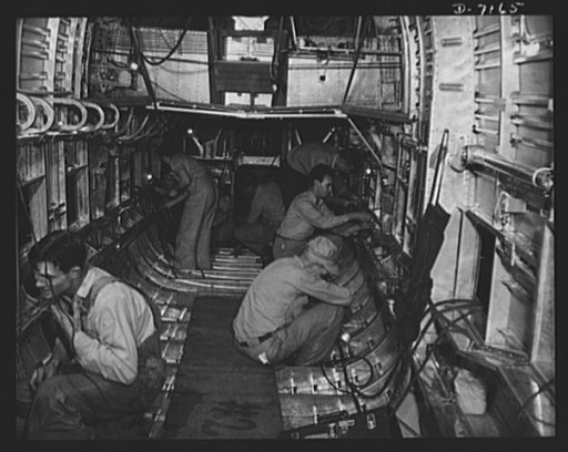 Production. B-24 bombers and C-87 transports. Installing fittings and operating equipment in the body of a consolidated transport plane under construction in a Western plant. View is looking forward from the tail fuselage. Note how the wing center section (top center) passes through the plane body. 