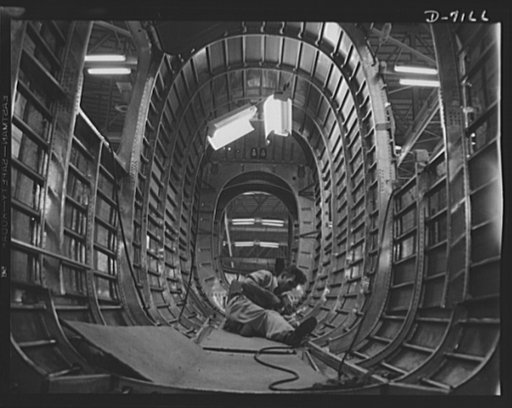 Production. B-24 bombers and C-87 transports. Structural parts of a consolidated transport plane are installed in the "tunnel" of a tail fuselage section in a Western plant. This new transport, an adaptation of the B-24 bomber, is known as the C-87, and carries one of the greatest human or cargo loa