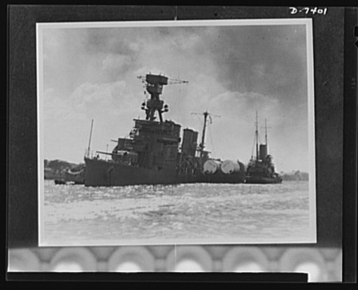 Pearl Harbor bombing. USS Raleigh. Torpedoed and bombed, the 7,050 ton light crusier USS Raleigh is held afloat near her anchorage in Pearl Harbor by a barge. The capsized USS Utah is in the background. The Raleigh rejoined the fleet months ago