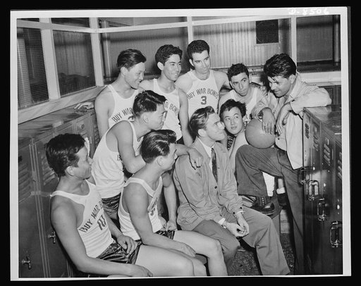 Coach Edwin Firiera, holding ball, gives his near pond team a pep talk in the locker room prior to their first league game. Seated with the players is assistant to the personnel officer at the Pearl Harbor Yard, Harry Brownell. This team is one of those composed of workers in the various shops at th