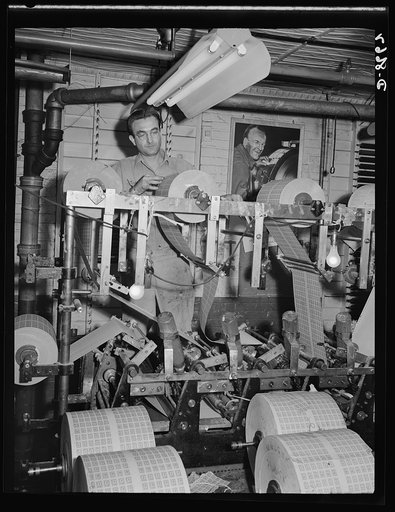 Printing war ration book 2. The coupons and covers flow through the collator where the pages and covers are assembled and glued. The coupons and covers leave the collator assembled in glued sheets aggregating four war ration books. Otto Krants inspects a roll of coupons on collator