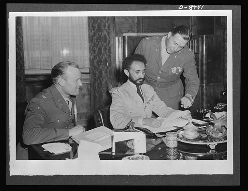 American military delegation calling on Haile Selassie. Poring over official papers. At the left of His Majesty, Haile Selassie, Emperor of Ethiopia, is Colonel Bishop, while at the right, standing, is Colonel Clark. These pictures are the first to be taken for publication since His Majesty's return