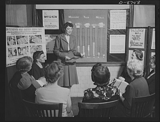 Preparation for point rationing. Miss Elizabeth Law, who teaches an adult homemaking class at Mckinley High School, Washington, D.C., explains the use of war ration book two to a group of homemakers at the school. The relationship of balanced diets to point-rationed foods is taught to adult classes 