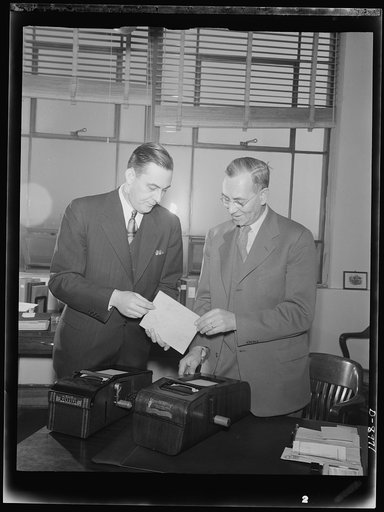 Plywood autographic registers. Plywood used in the new "Victory" model autographic registers is inspected by Nathaniel G. Burleigh (right), director of Service Equipment Division of War Production Board (WPB), and a company representative. The old model (left) contains seventeen and a half pounds of