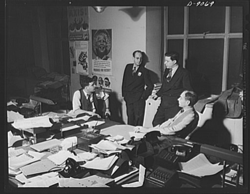 Office of War Information News Bureau. George McMillan, assistant chief of the OWI news bureau, talks over a program for a series of releases on inflation with Herb Plummer, standing at his right, Jack Durham and Joe Polakoff. When a series of releases is planned, the news bureau schedules them, oft