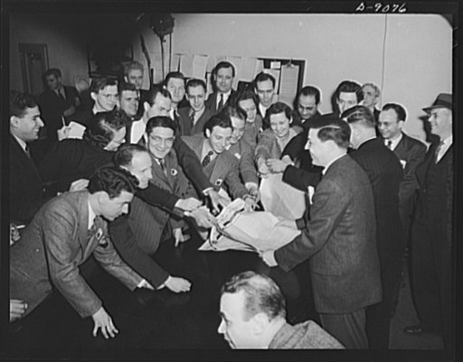 Office of War Information news bureau. Smiling unnaturally, some of the newsmen in OWI busy press room grab for a handout giving point values on canned goods from George (fatso) McMillan, assistant chief of the news bureau. McMillan has tried to make the news bureau work like a newspaper, has a repu
