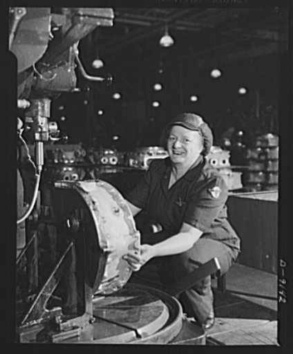 Clamping a supercharger housing into place underneath a radial drill calls for a "no-nonsense"-type of garment! This woman worker is correctly attired in a navy blue two-piece work uniform, and has her hair well under control