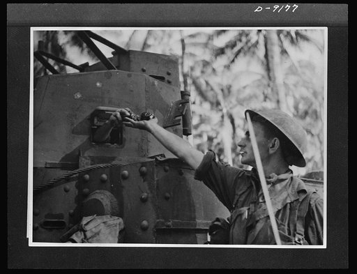 During the thick of the fighting at Buna, an Australian infantryman receives a handful of grenades from a fellow soldier inside the tank. American tanks manned by Australian crews, carried large quantities of grenades which were distributed to the infantry. This picture was made during the actual fi