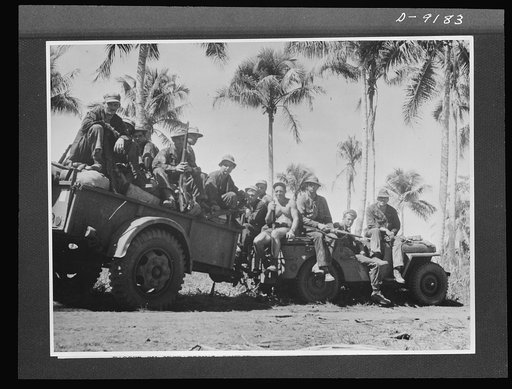Australia in the war. Men and supplies go to the front line at Buna. The trailer is hauled by an American jeep, one of the many uses which the versatile little vehicle has been put to in New Guinea