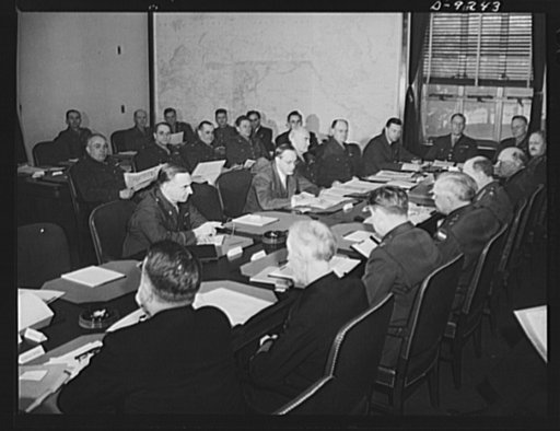 Combined Munitions Assignments Board. Combined Munitions Assignments Board at weekly meeting in Washington, with Chairman Harry Hopkins presiding. Staff officers in the background, attend the meetings. Seated at the conference table clockwise are the following: Major General L.D. Clay (American); Ha