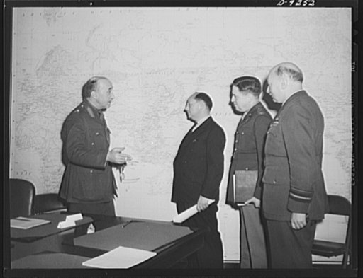 Combined Munitions Assignments Board. American and British officials of the Combined Munitions Assignments Board discuss their problems before the large world map in the conference room of the board in Washington. Left to right are: Lieutenant General G. N. Macready (British); Dr. I. Lubin (American