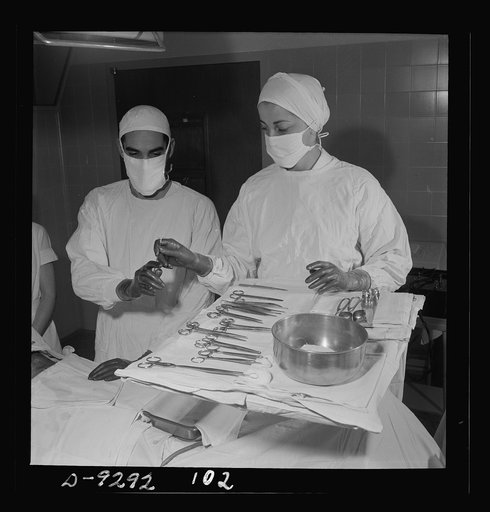 Nurse training. Assisting at an operation, a nurse hands a threaded needle to the surgeon who is about to perform an emergency tracheotomy
