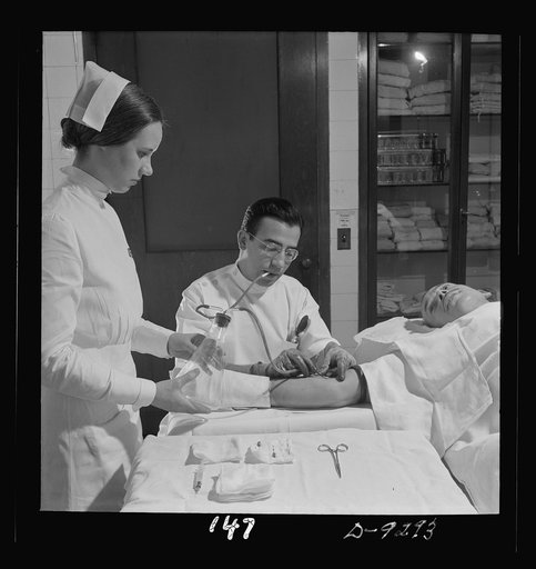 Nurse training. A nurse assists the doctor, who is inserting a needle in a patient's arm prior to a blood transfusion