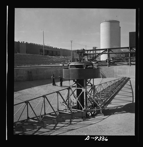 Production. Magnesium. Huge clarifier rakes stretch out like giant arms at Basic Magnesium's plant in the southern Nevada desert. One of the ore storage silos, eighty-four feet high, is in the distance