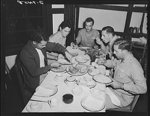 An American flying squadron in India. Just like home. The boys pitch to and go after the roast duck and vittles. Note the white tablecloth and flowers which is the custom at dinner in the "Hump Happy Tavern." Left to right are: Lieutenant R.J. Fruda, West Palm Beach, Florida; Lieutenant Joe H. Deer 
