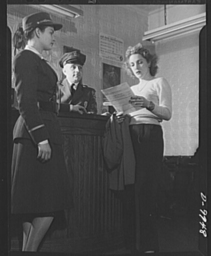 Safe clothes for women war workers. Looking over the job application blank, Eunice herself gets the once-over from guards at the Bendix Aviation Plant. She may be qualified for a job, but she'll have to change her style of dressing when she's hired. Bendix Aviation Plant, Brooklyn, New York