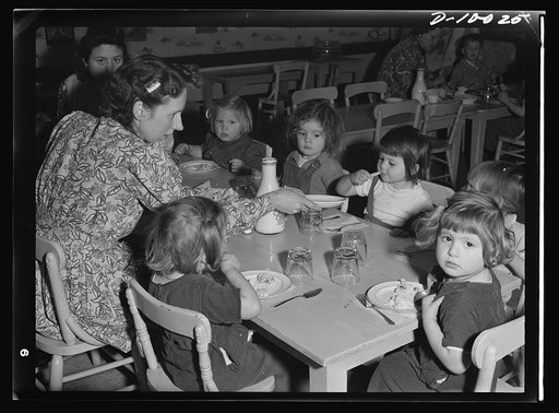 War workers' nursery. A young supervisor at the Bella Vista Nursery School in Oakland, California, eats luncheon with the smallest to prevent dawdling over food