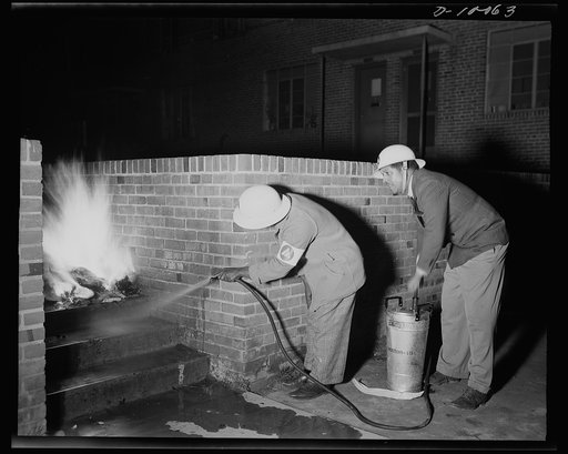 Office of Civilian Defense workers help protect nation's capital. Ever on the alert during patrol, the air raid warden is first to the scene of any action in his sector. Using a wall as a shield from the intense heat, these wardens operate a stirrup pump in extinguishing an incendiary fire during a 