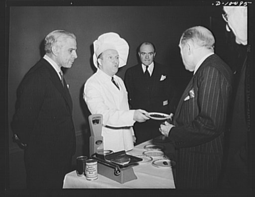 The Ambassador of Greece, Cimon P. Diamantopoulos watches as Representative Sol Bloom, chairman of the House Committee on Foreign Affairs accepts a plate of food, which had first been dehydrated, then rehydrated, at a luncheon held in observance of the second anniversary of lend-lease, on March 11, 