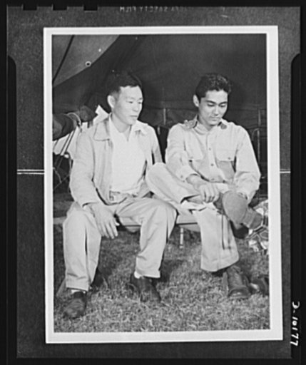 Japanese-American volunteers. There's quite a difference between sneakers and a pair of heavy GI boots, Mitsuru Doi, eighteen, of Kauai, finds out. He was the first to put on the uniform of an American soldier. Looking on is a fellow inductee, Shuichi "Pete" Sakamoto, thirty-four, who before his ind