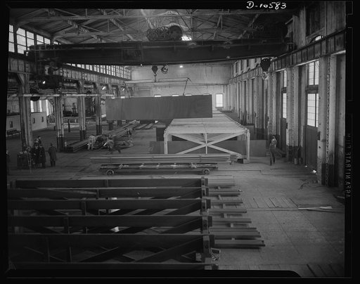 Denver, Colorado. Interior of a once-abandoned railroad machine shop, now producing fabricated steel parts for the hulls of escort vessels, showing an overhead crane which once lifted switch engine boilers and old box car axles, now moving a heavy steel plate which will become the sturdy belly of a 