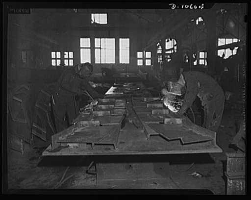 The interior of a shipbuilding plant, showing men working with acetylene torches
