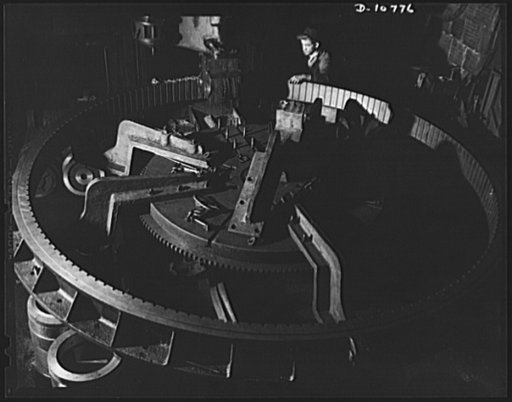 Close-up showing bracing arrangement on gear cutter. Giant arms holding gear in place are changed to adjust the rotating gear to the cutting mechanism. The job takes three to six weeks of day and night operation for completion. This is one of many highly specialized big precision jobs the converted 