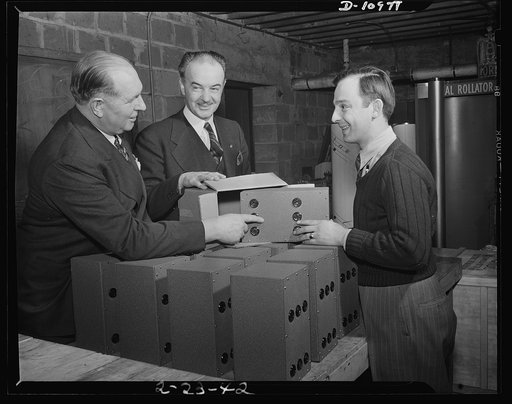 Minneapolis. The job's done and Peter Dockas, right, who by his ingenuity transformed the basement of this appliance shop at 2622 East Lake Street, Minneapolis, into a war industry, smiles. Dockas today was packaging the last of 150 radio control devices manufactured for the U.S. Army Signal Ccorps,