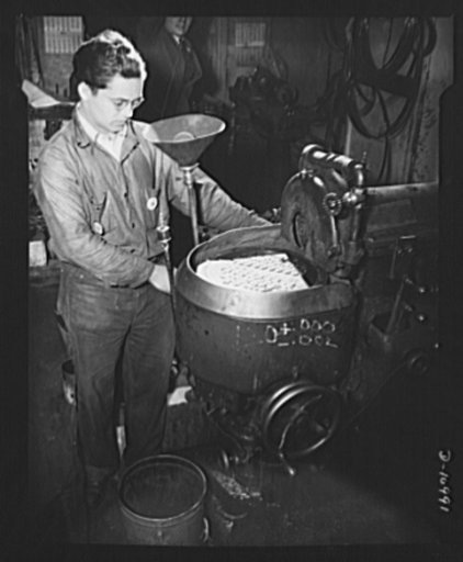 Grinding aircraft parts (one with inverted lamp shade). Tiny parts for aircraft are here being surface ground by a small machine shop in New York City whose peacetime products are industrial saws and knives. The same skill and machinery needed to produce saws and knives is thus being turned to the j
