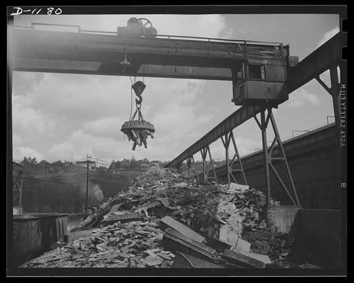 Steel manufacture, Allegheny-Ludlum. Back into production go these carloads of scrap metal. The melting of alloy steels for defense work requires that steel mill scrapyards such as this be constantly filled. The overhead magnet deposits the scrap in a loader which carries it to the open hearth furna